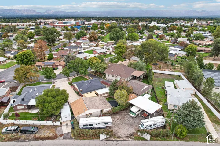 Aerial perspective featuring an expansive lot with a detached metal carport, gravel surfacing, mature trees, and a mountain range backdrop