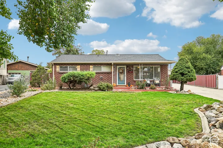 Brick exterior facade, asphalt shingle roof, front entry covered porch, manicured lawn, and stone landscaping border