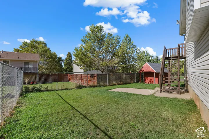 Rear yard featuring a chain-link and wood privacy fence, concrete patio, detached shed, and exterior staircase