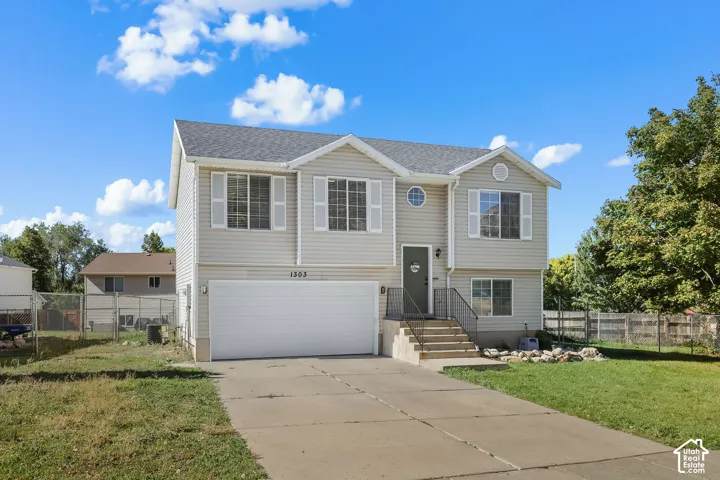 Split-level exterior with vinyl siding, dual-gable roofline, two-car garage, concrete driveway, and iron-rail front steps