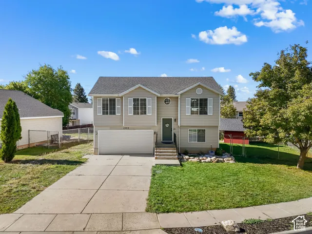 Split-level exterior featuring light-toned horizontal siding, a two-car attached garage, asphalt shingle roofing, and a front concrete driveway