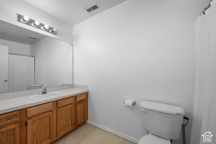 Bathroom featuring wood cabinetry, solid-surface vanity countertop with an integrated basin, full-width wall mirror, and four-bulb vanity light fixture