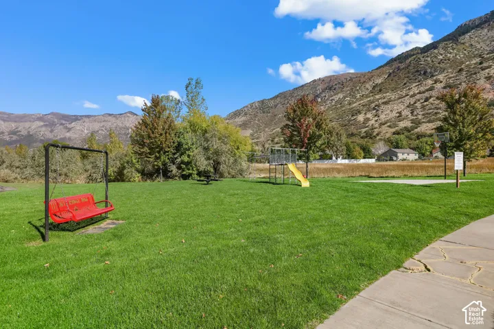 Expansive lawn featuring a swing set, slide, basketball hoop, and mountainous backdrop