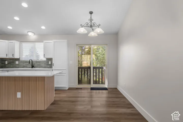 Kitchen featuring a center island with slatted wood-finish paneling, white shaker-style cabinetry, a gray tile backsplash, recessed lighting, and wood-finish flooring