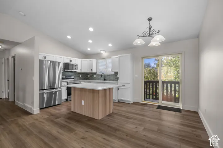 Kitchen featuring white cabinetry, wood-finish flooring, a central island with a light wood-finish base, stainless steel appliances, and a glass-paneled sliding door