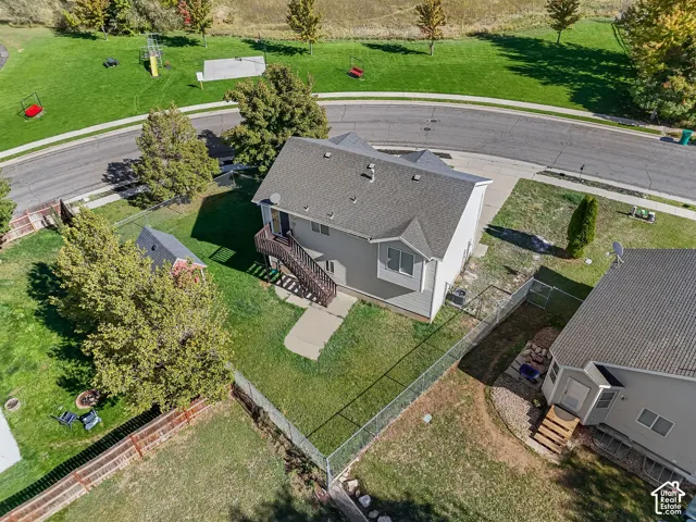 Aerial view of a residential property featuring an elevated wood deck, a fenced-in backyard, a detached storage structure, and a concrete walkway