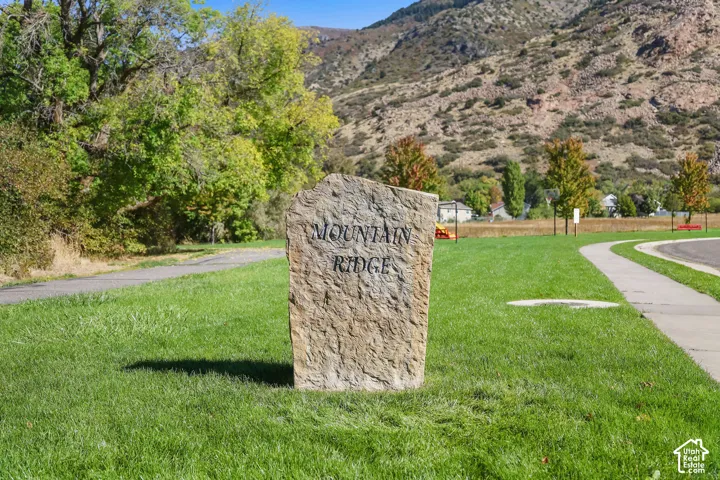 Natural stone monument featuring carved lettering, situated on a manicured lawn with paved walkways and a mountain backdrop