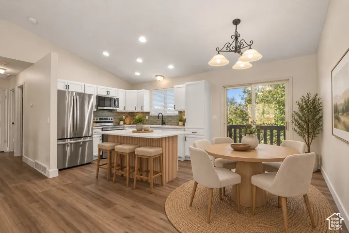 Kitchen featuring white cabinetry, wood-finish flooring, a central island with a stone-top surface, stainless steel appliances, and sliding glass doors