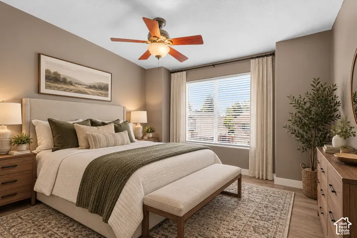 Neutral-toned room featuring wood-finish flooring, a centrally mounted ceiling fan with integrated light fixture, and a large window with horizontal blinds