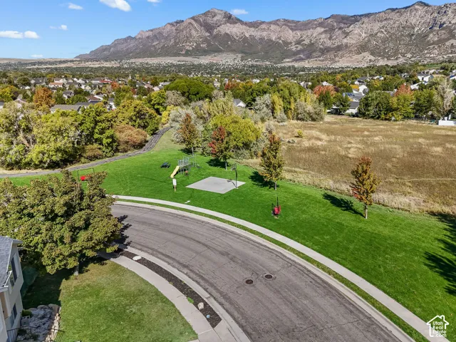 Expansive green space featuring a paved basketball court, playground equipment, and mature trees against a mountain backdrop