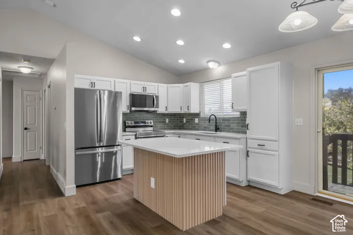 Kitchen featuring white shaker cabinetry, stainless steel appliances, a center island with a ribbed wood-finish base and solid-surface countertop, and a tiled backsplash