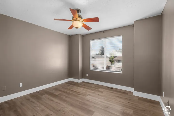 Interior room featuring wood-finish flooring, a multi-blade ceiling fan with integrated lighting, and a window with horizontal blinds