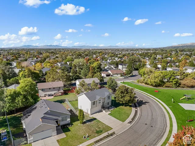 Aerial perspective of suburban residential property featuring multi-level construction, attached garages, paved driveways, and expansive mountain backdrops