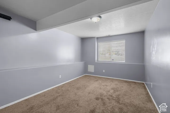 Neutral-toned interior space featuring wall-to-wall carpeting, a structural soffit, and a window with horizontal blinds