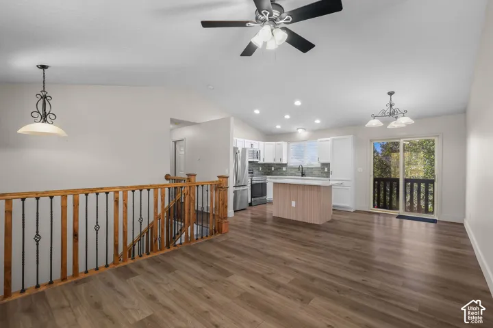 Open-concept space featuring vaulted ceilings, wood-finish flooring, a kitchen island with stone-surface countertop, recessed lighting, and a stairway with wood-and-wrought iron railing
