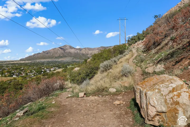 Natural hillside terrain featuring unpaved paths, native shrubbery, large rock formations, and mountain topography