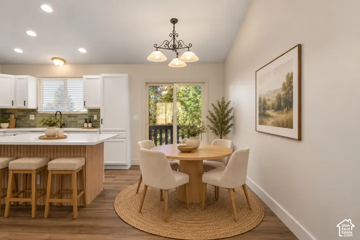 Kitchen featuring a central island with a slatted wood base and white countertop, recessed ceiling lighting, decorative wrought-iron chandelier, green tile backsplash, and a sliding glass door