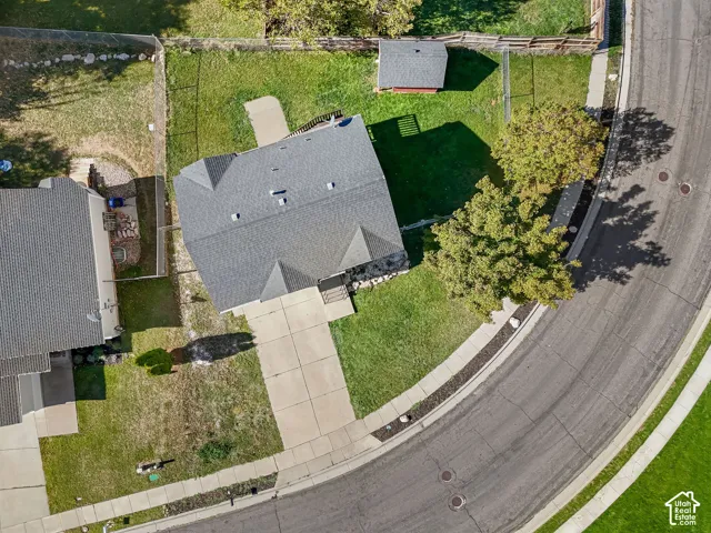 Aerial perspective of property featuring an asphalt shingle roof, concrete driveway, fenced yard, and detached storage structure