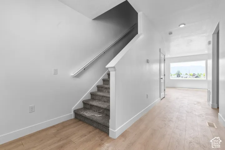Interior space featuring light wood-finish flooring, staircase with carpeted treads and white handrail, recessed ceiling lighting, and large window with mountain scenery
