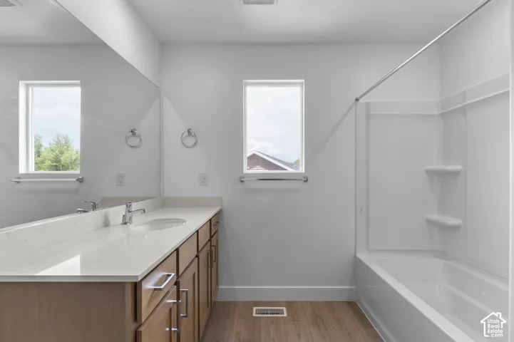 Bathroom featuring a wood-finish vanity with a light-toned countertop, integrated basin, oversized wall-mounted mirror, and a tub-shower combination with built-in shelving
