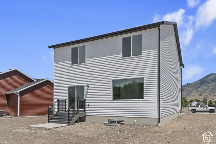 Two-story residence featuring white horizontal siding, a shed roofline, mountain backdrop, and a rear exterior staircase with black metal railings leading to a sliding glass door
