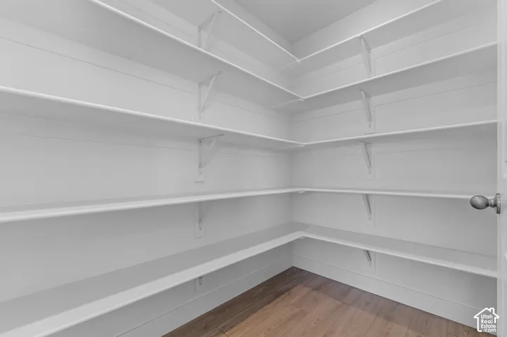 Walk-in pantry featuring white wrap-around shelving, support brackets, and wood-finish flooring