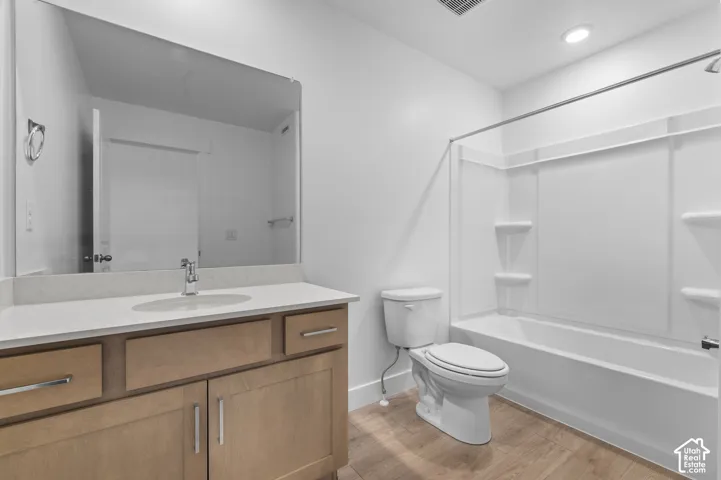 Bathroom featuring wood-finish cabinetry, a solid-surface vanity countertop with an integrated basin, a large wall-mounted mirror, wood-finish flooring, and a tub-shower combination with built-in shelving