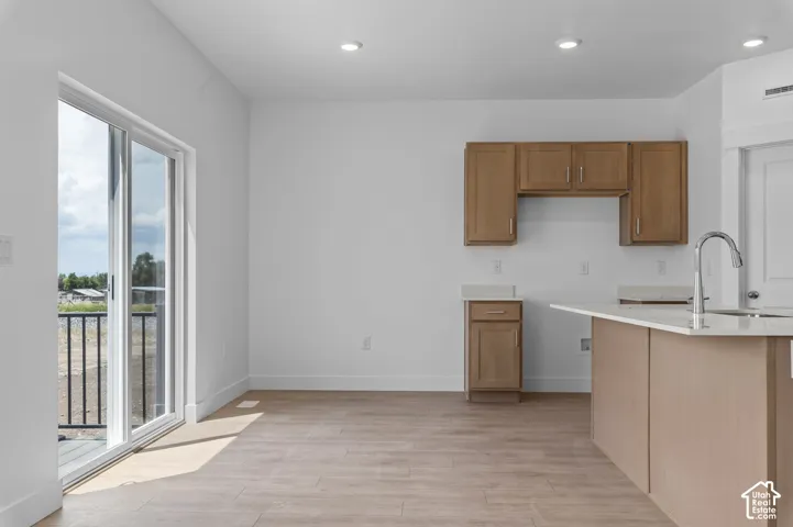 Kitchen featuring wood-finish cabinetry, neutral solid-surface countertops, a stainless steel gooseneck faucet, recessed lighting, and sliding glass doors with access to an exterior deck