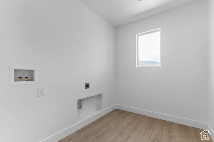 Utility room featuring wood-finish flooring, a recessed water supply box, a dedicated recessed dryer vent, and a single window