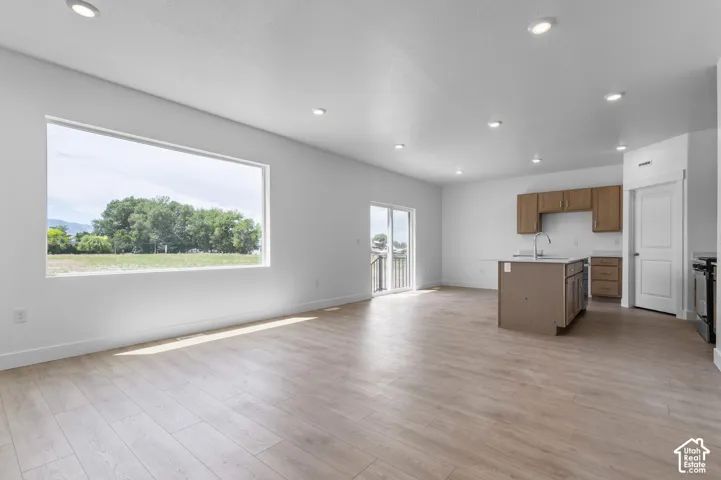 Open floor plan featuring wood-finish flooring, recessed lighting, a large picture window, a kitchen island with a built-in sink, and sliding glass doors