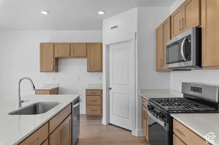 Kitchen featuring light-finish cabinetry, stone-surface countertops, an integrated island with an undermount sink, recessed lighting, and stainless steel appliances