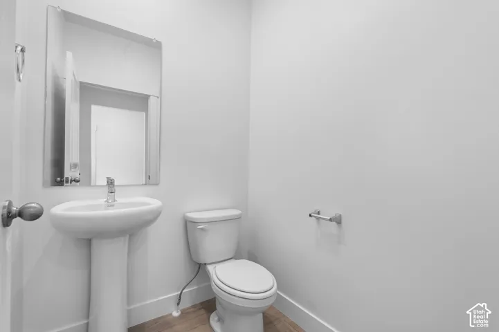 Pedestal sink with chrome faucet, wall-mounted mirror, and wood-finish flooring