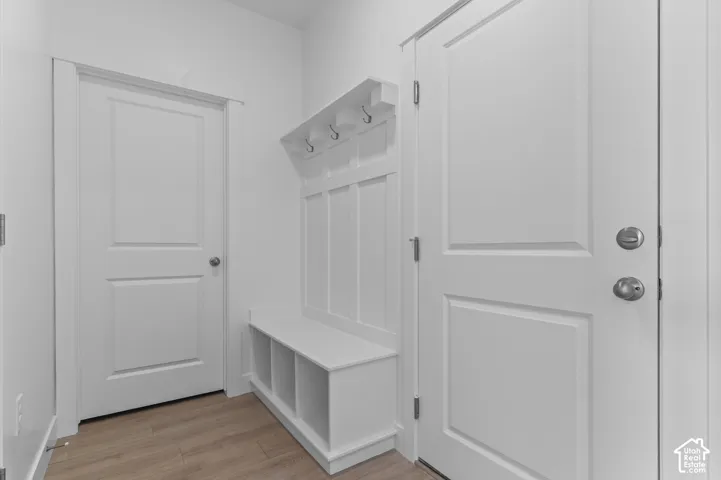 Built-in mudroom bench featuring wainscoting, integrated coat hooks, and lower storage cubbies, complemented by wood-finish flooring and solid-core paneled doors