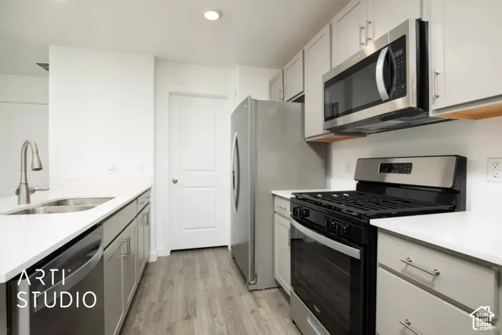 Kitchen featuring light-colored cabinetry, stainless steel appliances, white solid-surface countertops, dual-basin sink with a gooseneck faucet, and wood-finish flooring