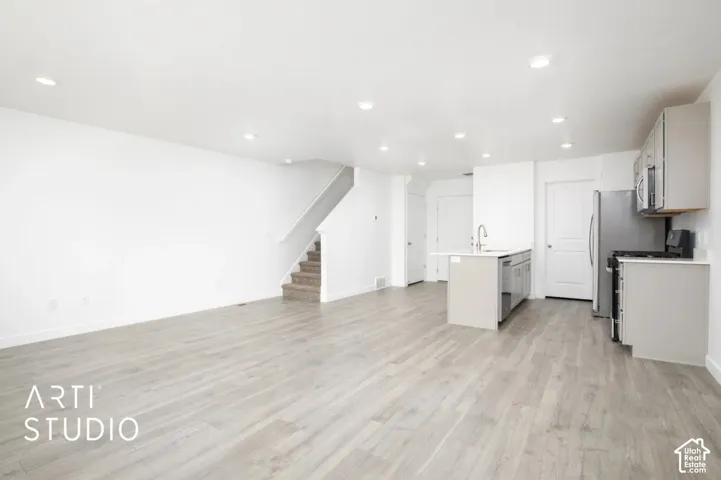 Open-concept interior featuring light wood-finish flooring, recessed lighting, a center kitchen island with a stainless steel faucet, and cabinetry with stainless steel appliances