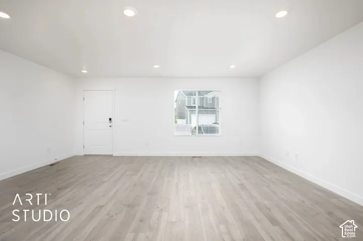 Neutral interior space featuring wood-finish flooring, recessed lighting, and a single-panel door