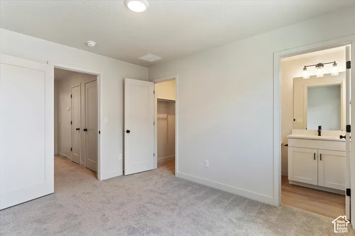 Neutral wall tones, wall-to-wall carpeting, shaker-style interior doors with matte black hardware, reach-in closet, and bathroom featuring a vanity with a white countertop and multi-bulb light fixture