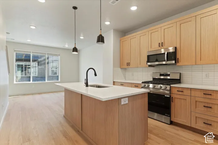 Kitchen featuring flat-panel wood cabinetry, white stone-finish countertops, subway tile backsplash, stainless steel appliances, and a center island with a matte black faucet