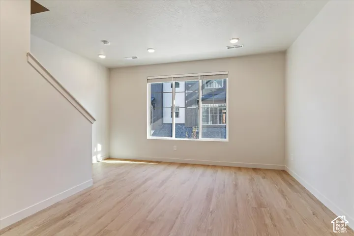 Neutral interior space featuring wood-finish flooring, recessed lighting, and a large window with roller shades