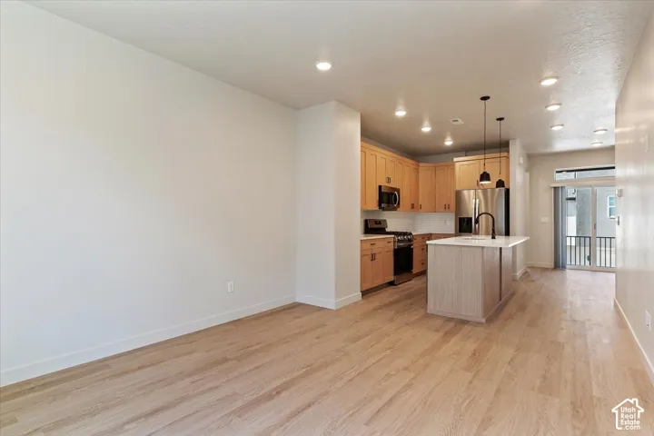 Kitchen featuring light wood cabinetry, stone countertops, stainless steel appliances, a central island with a matte black faucet, and wood-finish flooring
