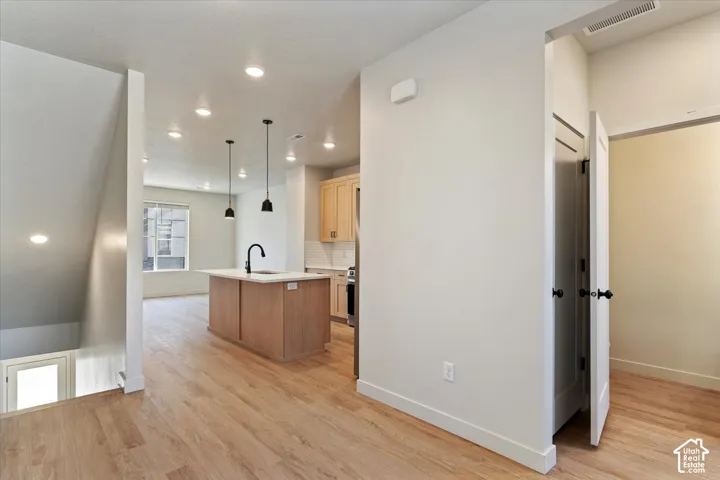 Kitchen featuring an island with a stone countertop, wood-finish cabinetry, recessed lighting, pendant fixtures, and wood-finish flooring