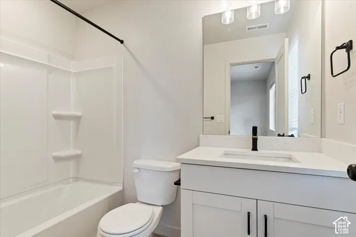 Bathroom featuring a white shaker-style vanity with stone-composite countertop, matte black faucet, integral vanity mirror with overhead glass light fixture, and a white tub-shower surround