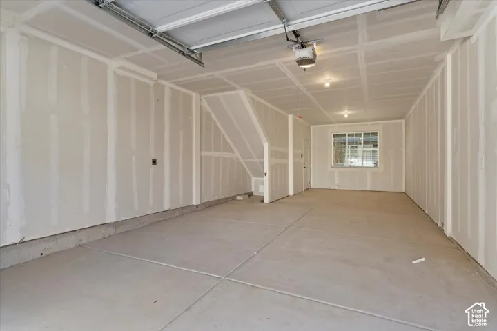 Attached garage featuring drywall finish, concrete flooring, single-pane window, and overhead door mechanism