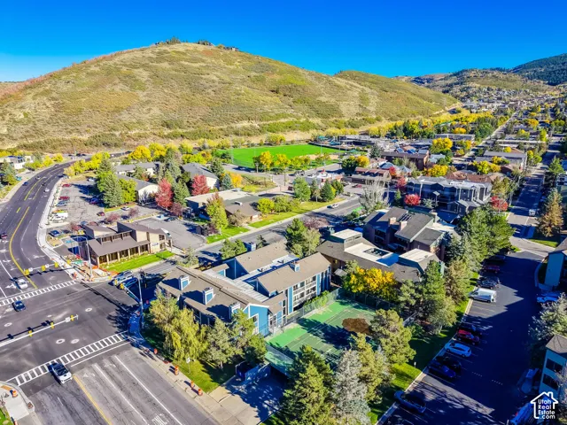 Aerial perspective of a multi-level residential complex featuring a dedicated tennis court, structured parking, mature trees, and mountainous terrain