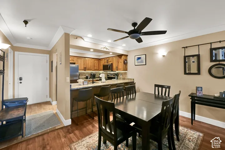 Kitchen featuring wood cabinetry, stone backsplash, quartz countertops, a breakfast bar, and wood-finish flooring