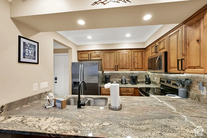Kitchen featuring wood cabinetry, natural stone countertops, under-cabinet lighting, stainless steel appliances, and a tiled backsplash
