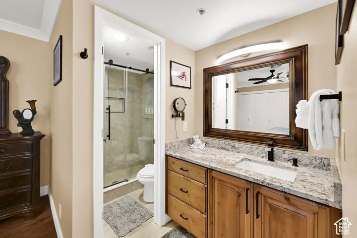 Bathroom featuring a wooden vanity with stone countertop, rectangular undermount sink, matte black hardware, and an enclosed shower with glass sliding door