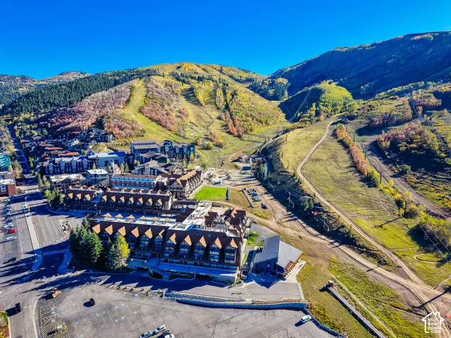 Aerial perspective of a multi-story lodge featuring a pitched roofline, stone and wood-tone siding, paved surface parking, and proximity to mountainous terrain