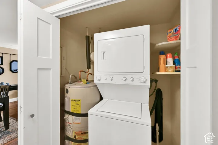 Utility closet featuring white bifold doors, a stacked washer and dryer unit, a residential water heater, and built-in shelving