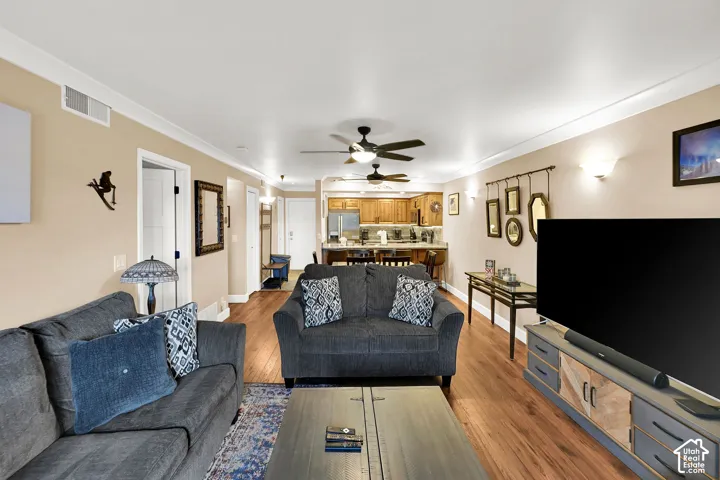 Open-concept floor plan featuring wood-finish flooring, dual ceiling fans, crown molding, and a kitchen equipped with built-in cabinetry